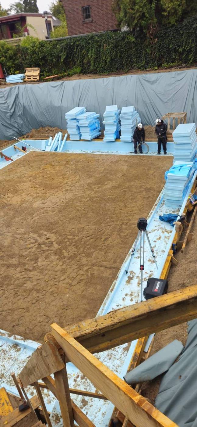 Zwei Bauarbeiter in einer Baugrube mit Dämmplatten und Nivelliergerät